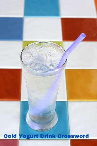 A cold yogurt drink in a tall glass next to a partially solved crossword puzzle.